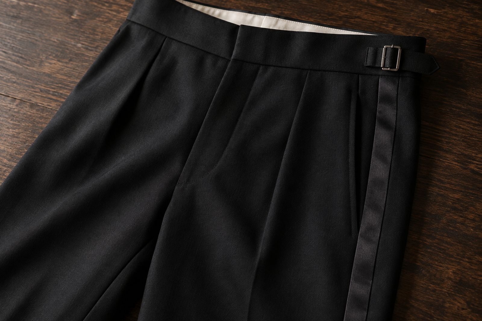 Black dinner suit trousers with silk braid down the side seam, a side adjuster and no belt loops.