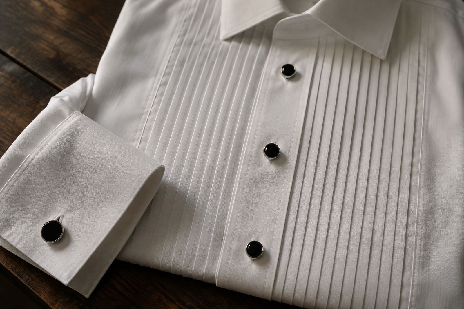 Pleated bib of a white dress shirt with black onyx studs and a matching cufflink.