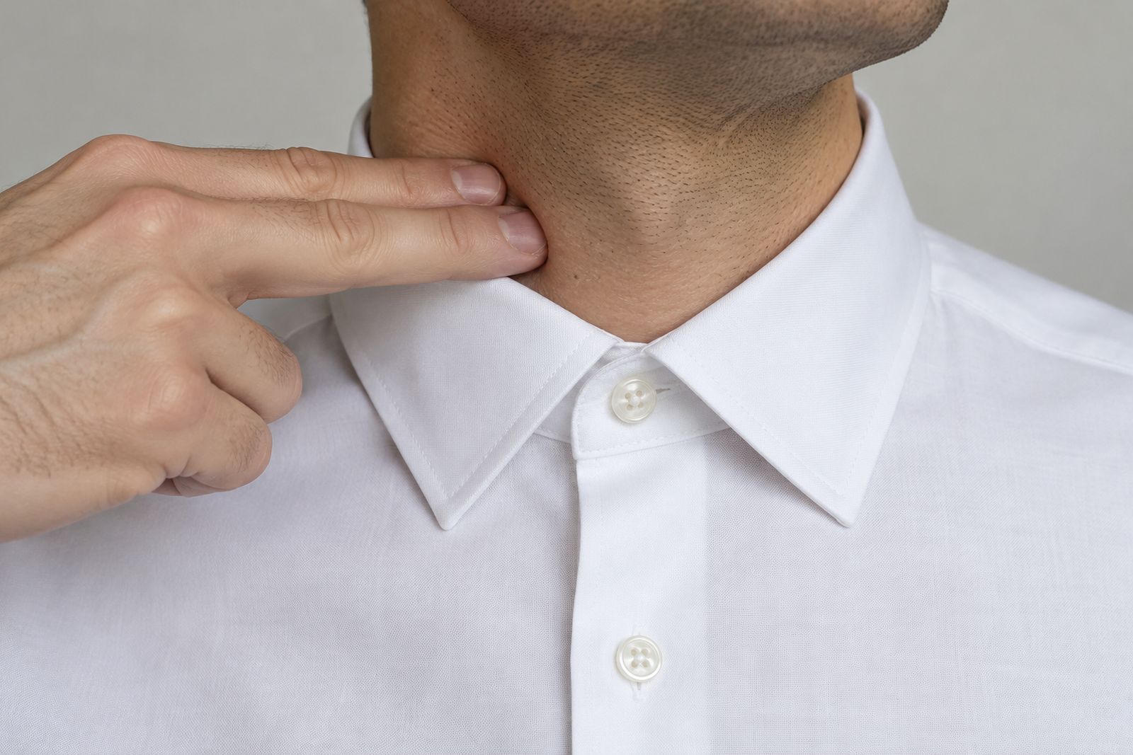 Two fingers slid flat between a buttoned white shirt collar and the side of the neck.