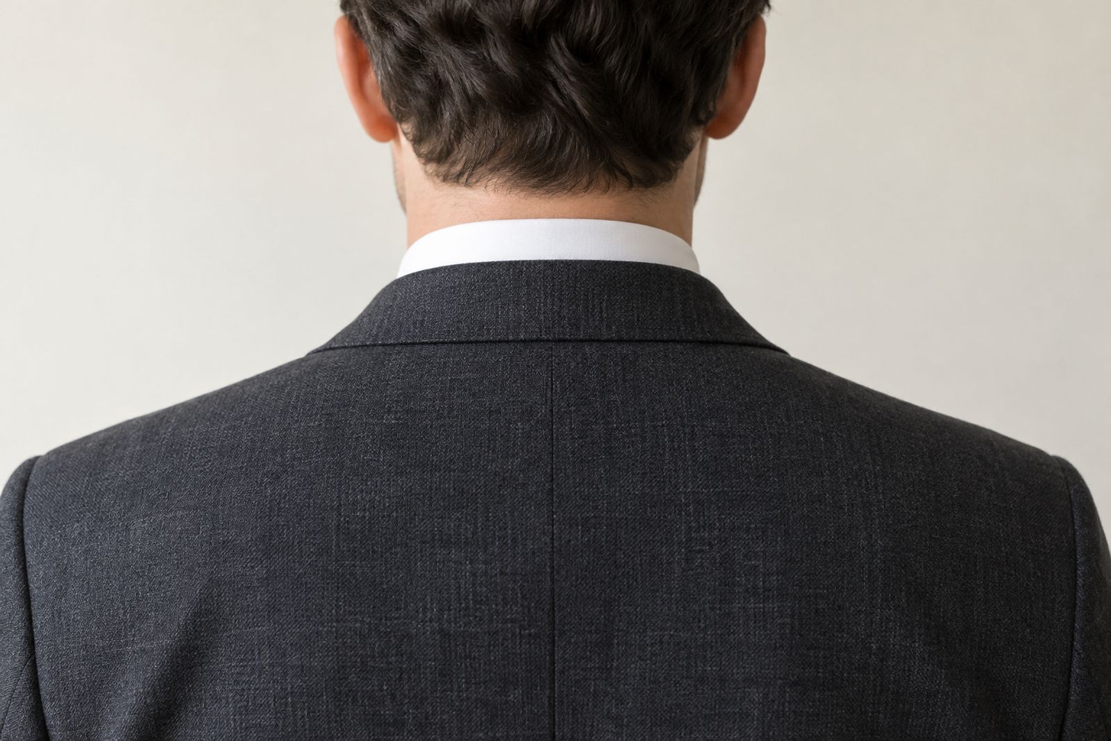 The back of a charcoal jacket collar sitting flat against the shirt collar, with a band of white collar showing above.