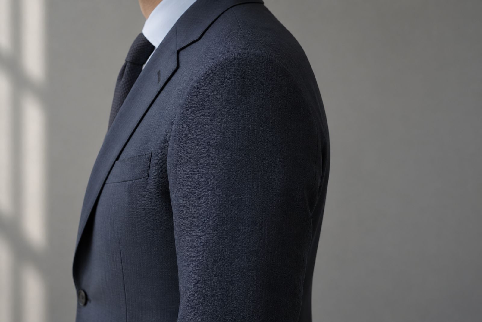 Side view of a navy suit jacket shoulder, the seam ending at the shoulder bone and the sleeve hanging smoothly.