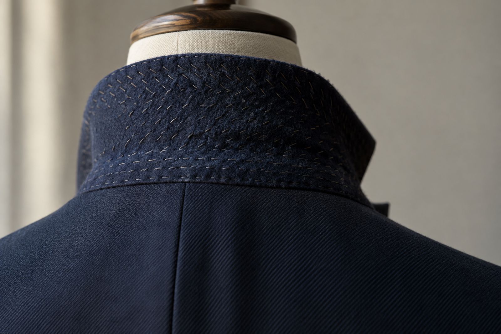A turned-up jacket collar showing navy melton felt with rows of small hand pad stitches.