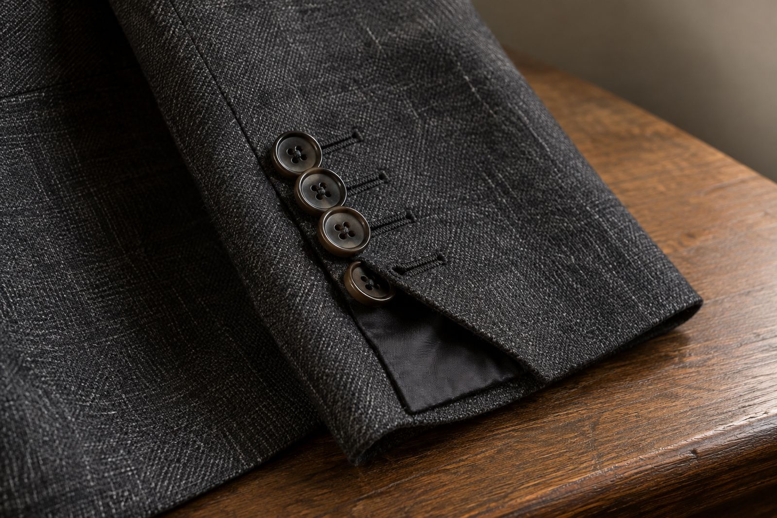 A charcoal jacket cuff with four working buttonholes, the last button undone so the vent opens.