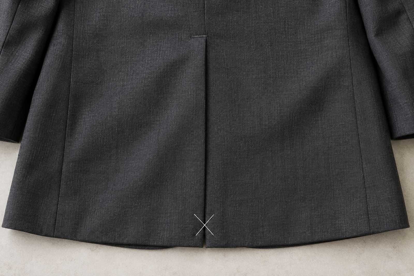 A loose white X-shaped tacking stitch holding the vent of a new charcoal jacket closed.