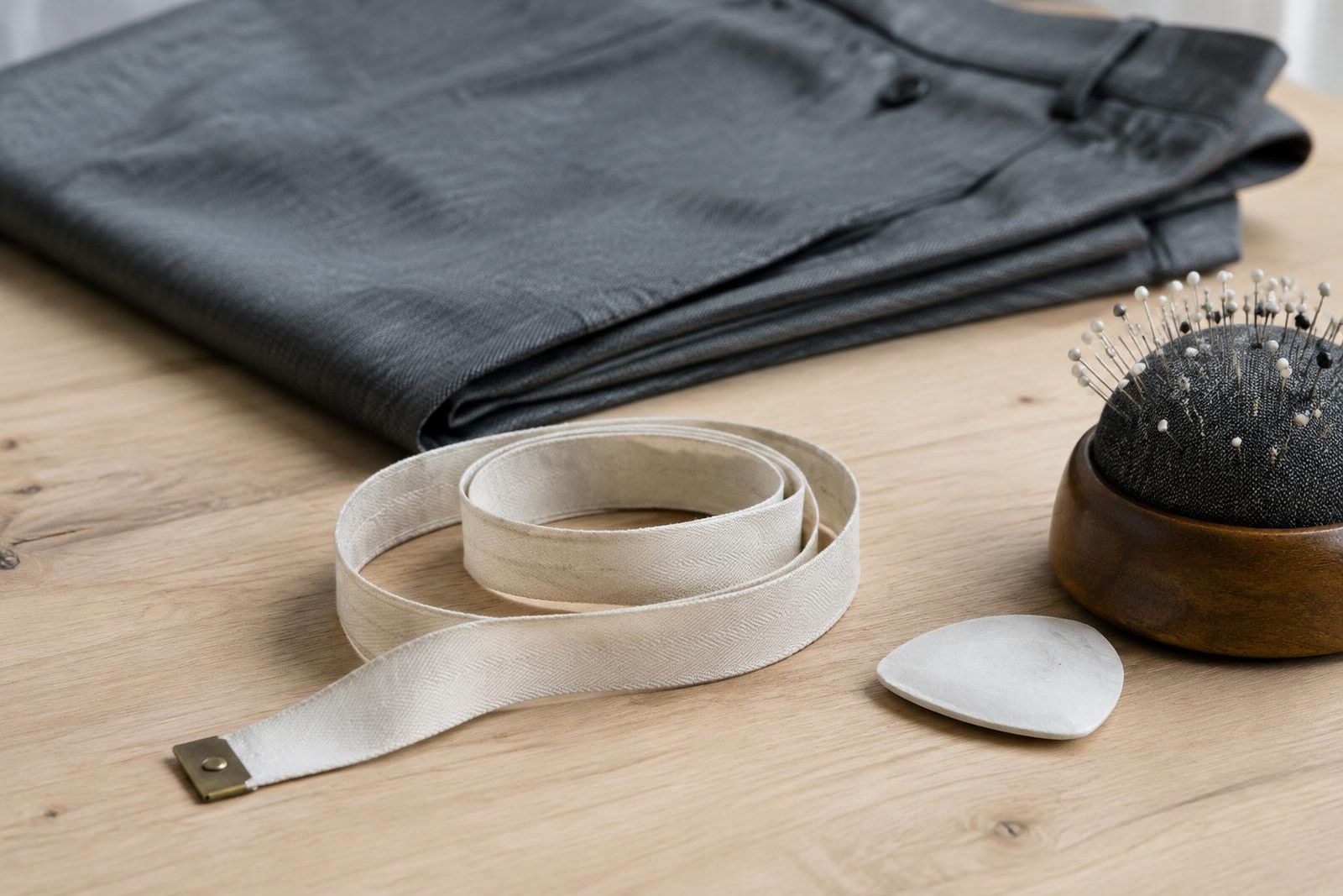 A tape measure, chalk and pincushion on an alteration counter beside folded gray trousers