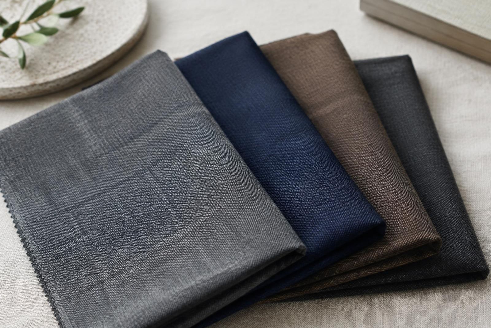 Folded gray, navy and brown wool suiting swatches fanned across a linen table